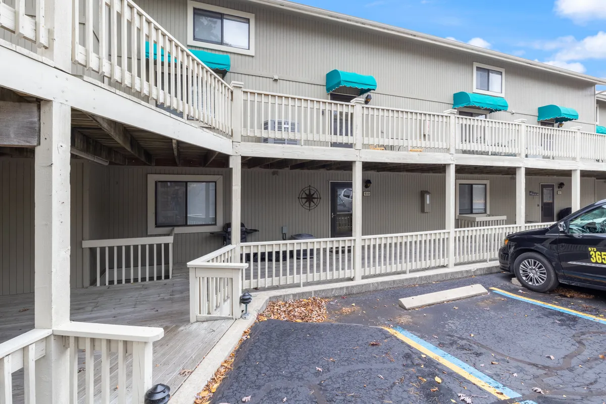 A welcoming balcony with teal awnings and wooden railings, overlooking the parking area. The compass wall decoration and outdoor seating create a relaxed, social vibe—ideal for unwinding after a day out.