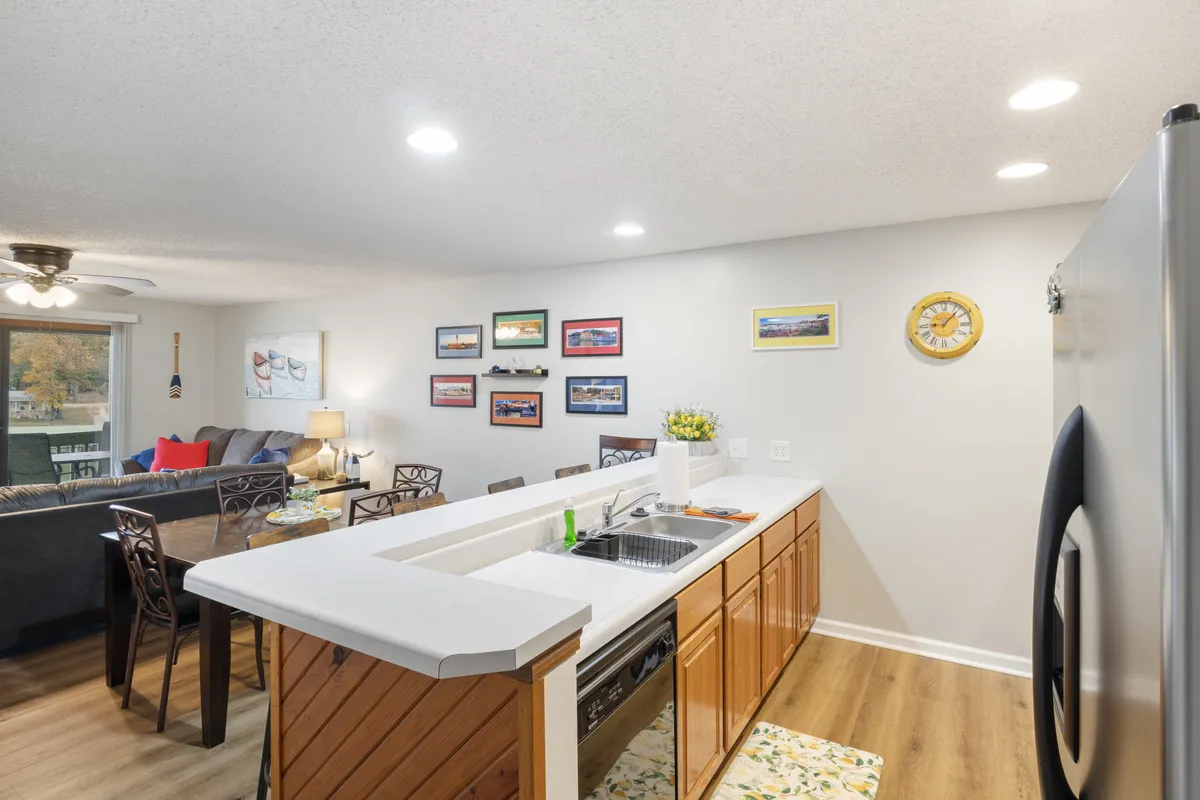 This interior image captures an inviting open-plan layout featuring a kitchen island, a dining table, wall art, and a glimpse of the living room seating. The dining table is ready for family meals or celebrations, while the kitchen island offers ample space for meal prep and casual dining. The overall mood is bright, social, and welcoming, with sunlight streaming in and cohesive decor throughout.