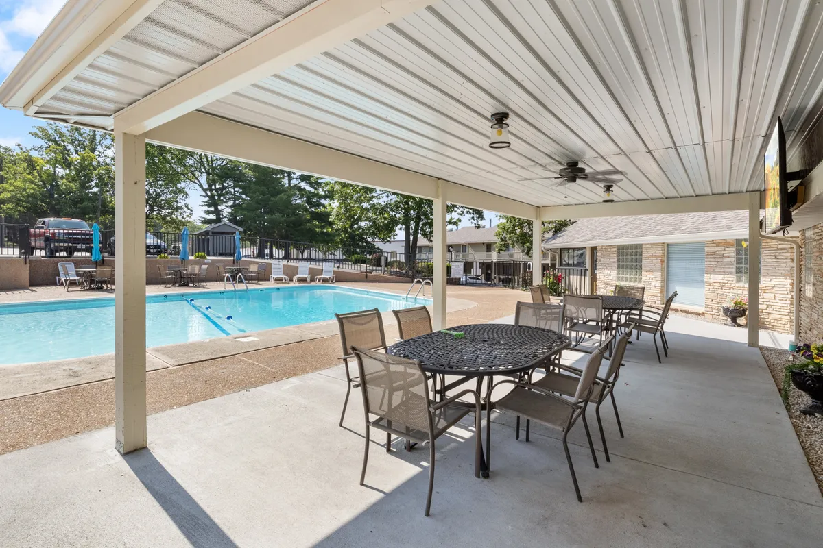 This exterior image captures a shimmering swimming pool surrounded by a spacious patio with a dining table, outdoor ceiling fan, and inviting lounge chairs. The setting suggests a relaxed atmosphere perfect for gathering with friends or family after a day on the lake or trails.