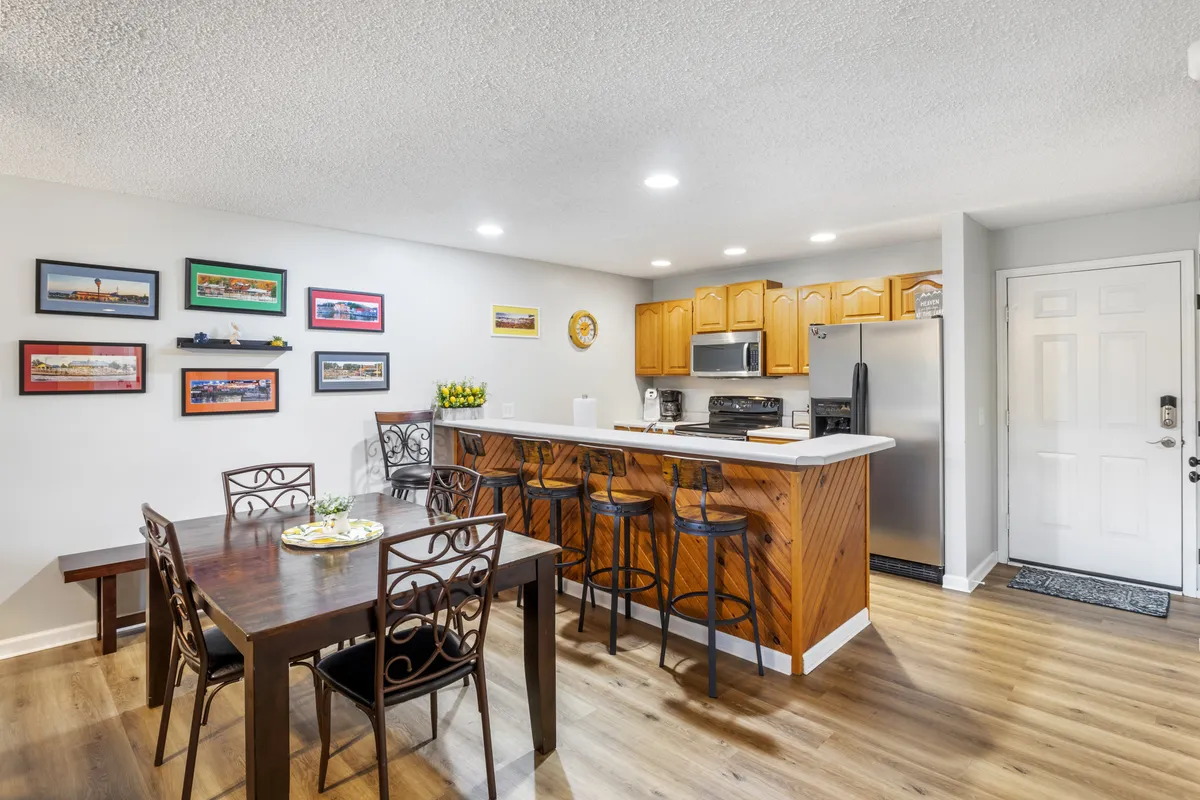 The image features a dining table adjacent to a kitchen island complete with bar stools and stylish wall art. The setting is designed for family meals, entertaining guests, and shared cooking, all within a cozy and communal atmosphere. Warm lighting and open sight lines encourage togetherness and effortless flow between dining and living spaces.