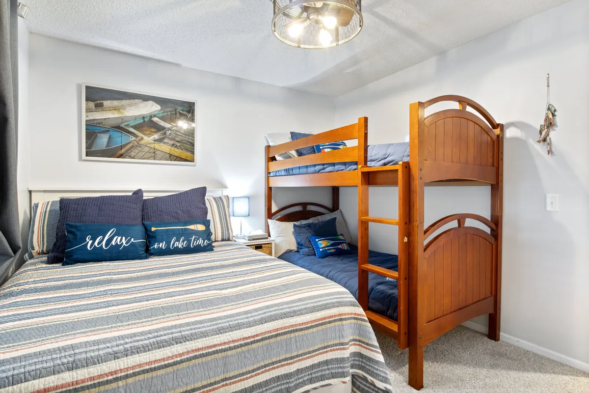 The scene features a large bed with decorative pillows and a cheerful bunk bed set, complete with playful accents and framed artwork. The room feels welcoming and flexible, ideal for both families and groups.
