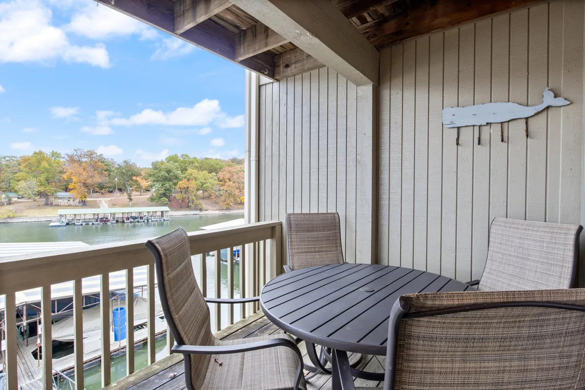 An exterior patio scene featuring a round table set for four, decorative whale art on the wall, and a water view in the background. The chairs invite guests to sit for alfresco dining, morning coffee, or an evening meal with lake views. The ambiance is serene and highlights the connection between indoor comfort and the scenic outdoors.