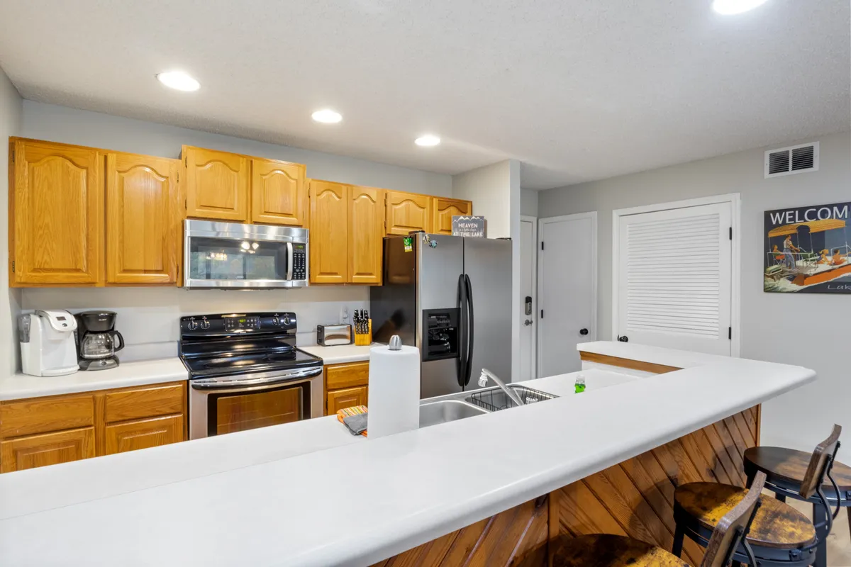 A warm, inviting kitchen interior with a prominent kitchen island, stainless steel appliances, wooden cabinetry, and decorative wall art. The space looks well-equipped, ideal for cooking and entertaining, and suggests a fully stocked kitchen experience. The lighting and decor create a cozy ambiance suitable for any meal from a quick breakfast to a celebratory dinner.