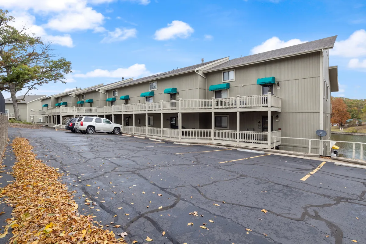 A wide shot of the building’s facade with a tree in autumn colors, parking area, and a glimpse of the water beyond. The pathway leads to the entrance, inviting exploration of the local area.