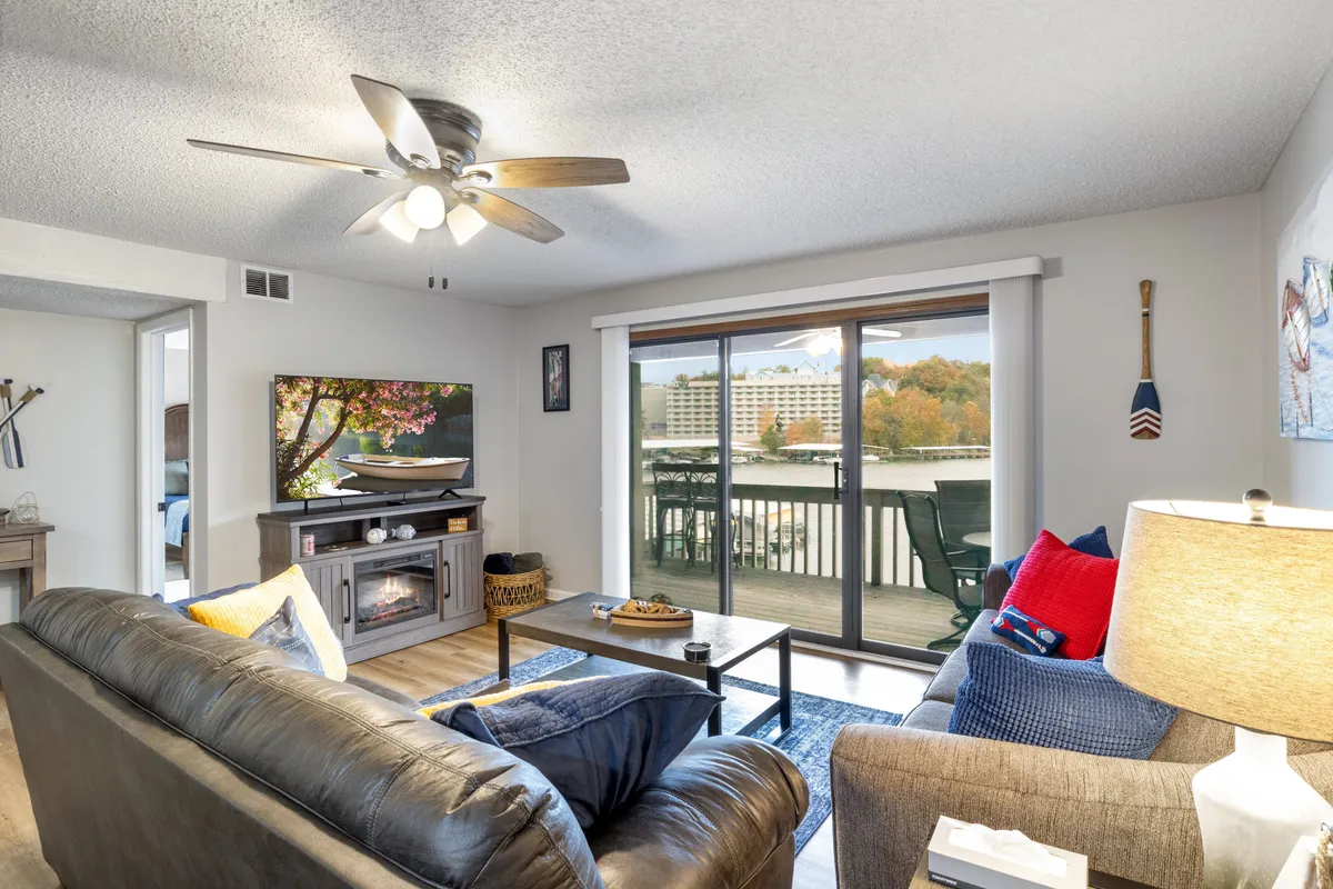 This image presents a plush leather sofa set near a large window, which offers a stunning view of the lake. Decorative wall art, a coffee table with decorative items, and a television with artwork create a cozy and welcoming living area. The warm, inviting furnishings and ample natural light suggest a space ideal for unwinding and gathering after a day at the lake.