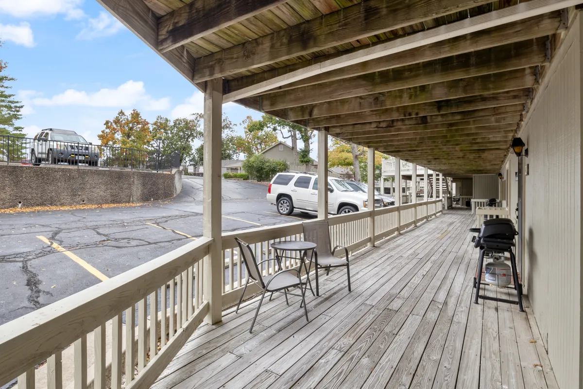 A wooden deck furnished with a table and chairs, accompanied by a grill. The deck overlooks greenery and offers a partial view of the outdoors, creating a serene space for relaxing, dining, or enjoying morning coffee. The scene suggests a tranquil lakefront ambiance and opportunities for both sunrise views and evening gatherings.